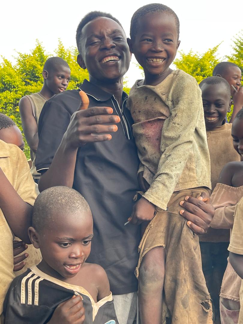 A caregiver laughing while carrying a smiling child surrounded by other children