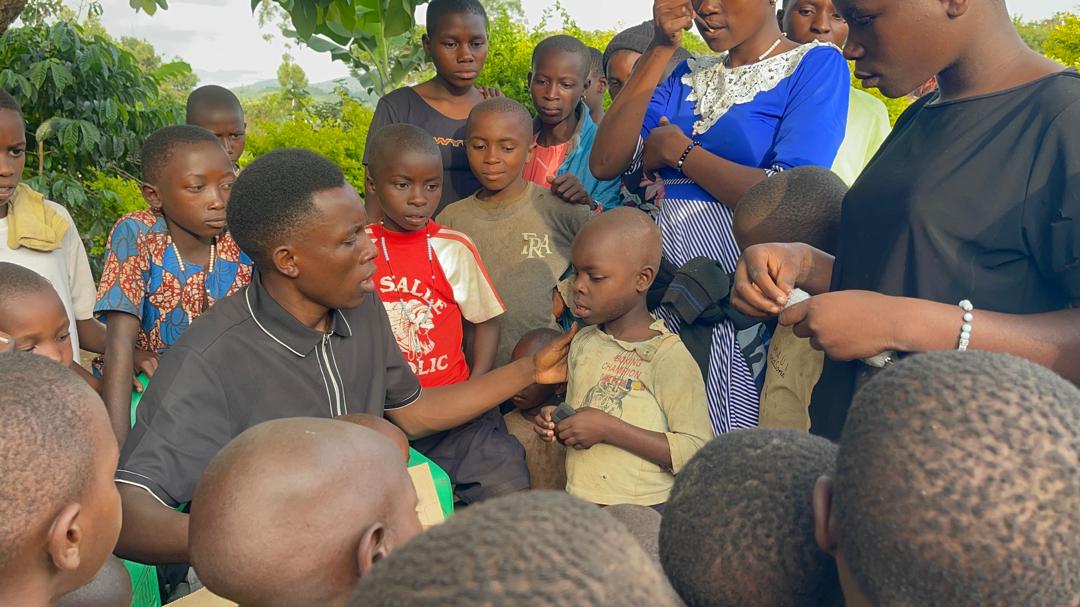 A caregiver teaching a circle of attentive children outdoors in Uganda